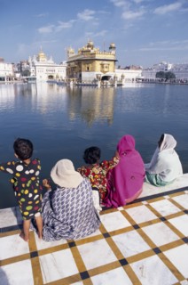 INDIA, Punjab, Amritsar , Women and children sitting on walkway beside sacred pool looking across