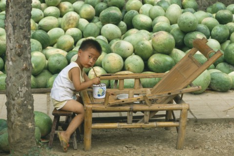 CHINA, Guizhou Province, Kaili, Liitle boy eating from bowl with chopsticks with large pile of