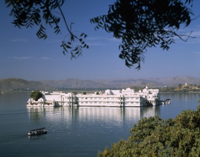 INDIA, Rajasthan, Udaipur, The Lake Palace framed by tree branches with white reflections on water