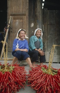 CHINA, Guizhou, Yuno, Two smiling female chilli vendors sitting on a pavement behind their chillies