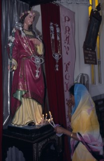 INDIA, Karnataka, Mysore, Indian woman lighting candles in front of statue of religious figure at