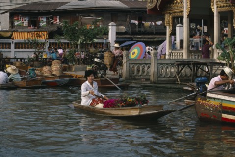 THAILAND, Bangkok, Floating Market, Woman rowing canoe containing flowers with woman on the jetty