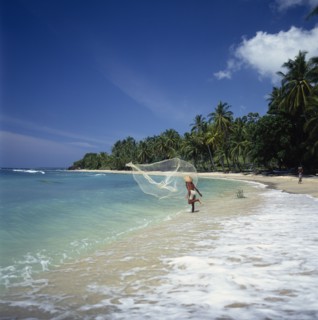 INDONESIA, Lombok, Mentiggi, Fisherman casting fishing net into sea from the surf on a coconut palm
