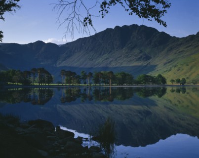 ENGLAND, Cumbria, Lake District, Buttermere.  Rugged hills and trees with mirror reflection in lake