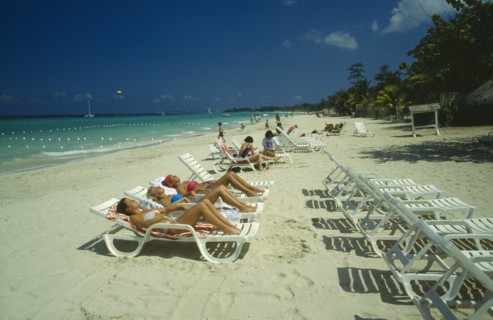 WEST INDIES,  Jamaica, Negril, Female tourists beach sunbathing on sun loungers facing away from