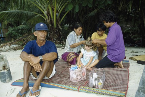 THAILAND, South, Koh Samui, Young Western girl on sandy beach having her hair braided by three Thai