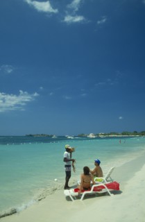 WEST INDIES, Jamaica, Negril, Man selling lobster to tourists on beach sitting on sun loungers by