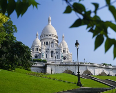 FRANCE, Ile de France, Paris, Sacre Coeur.  Exterior against blue sky partly framed by tree