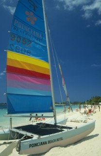 WEST INDIES, Jamaica, Negril, Catamaran with sail up on beach with tourists sunbathing and walking