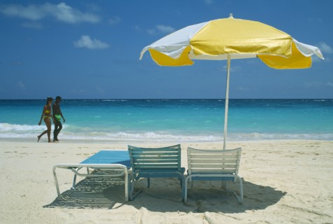 BERMUDA, Long Bay Beach, Tourist couple walking on beach by water past umbrella and sun loungers