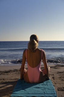 USA, Florida , Sunbathing, Young woman sitting on a sandy beach wearing a pink swimsuit with back