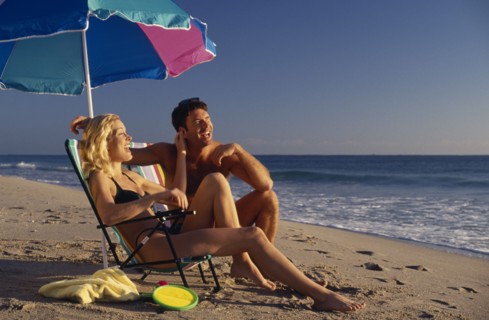 USA, Florida, Fort Lauderdale, A young couple sitting under a parasol on a sandy beach