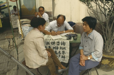 CHINA, Shaanxi, Xian, Professional letter writer with customers sitting at a desk outside the post