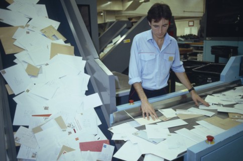 ENGLAND, East Sussex, Brighton, Mail sorting office.  Male worker sorting through letters on