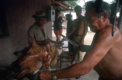 CUBA, Palma Soriano, Man standing at spit carving a whole roasted pig with a large knife