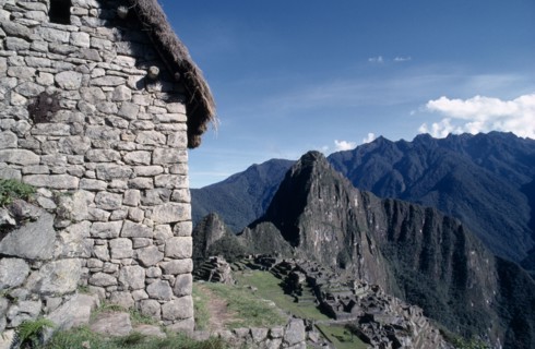 PERU, Cusco, Machu Picchu, View of the side of a stone built thatched house with ruins beyond