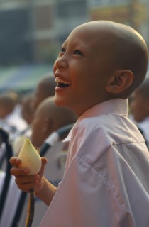 THAILAND, North, Chiang Mai, Laughing novice monk dressed in white holding a lotus flower during a