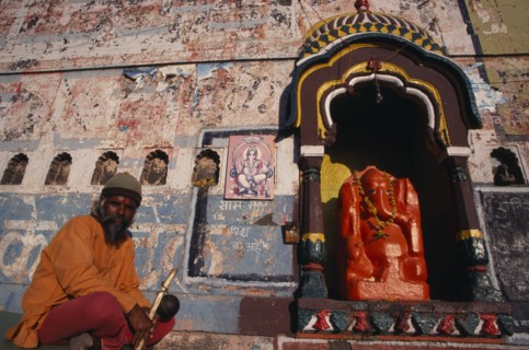 INDIA, Maharashtra, Nasik, Sadhu sitting beside shrine dedicated to Ganesh with orange painted
