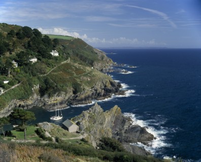 ENGLAND, Cornwall, South Cornwall . Rugged coastline with yachts in bay and houses on hillside