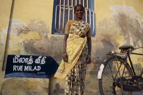 INDIA, Tamil Nadu, Pondicherry, Woman in a yellow sari standing in front of a yellow wall beside a