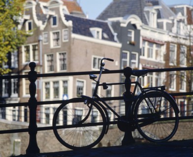 HOLLAND, North, Amsterdam, Bike parked against railings with traditional architecture behind.