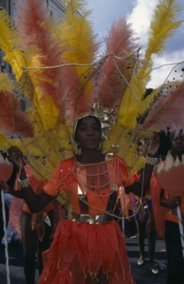 ENGLAND, London, Notting Hill Carnival. Woman in orange costume with orange and yellow feathers and