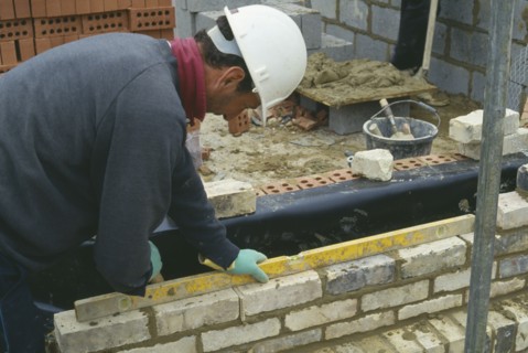 ARCHITECTURE, Construction, Bricklayer, Workman wearing a hard hat using a spirit level to lay
