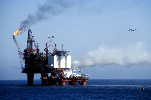 INDUSTRY, Factory, Oil Rig, Worker in a hard hat standing on the deck watching flames from burning