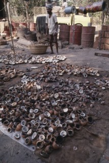 INDIA, Goa, Colva, Copra worker with piles of coconut shells in the foreground and oil drums behind