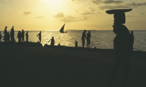 TANZANIA , Zanzibar, Zanzibar, People on the waterfront silhouetted against yellow sunset with dhow