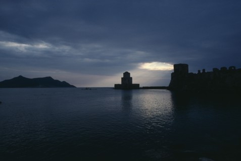 GREECE, Peloponnese, Methoni, View across the sea towards fortress ruins lit by evening sun rays