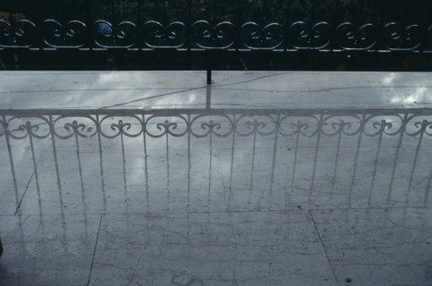 GREECE, Reflection, Decorative wrought iron balcony railings casting a shadow onto a pale wet floor