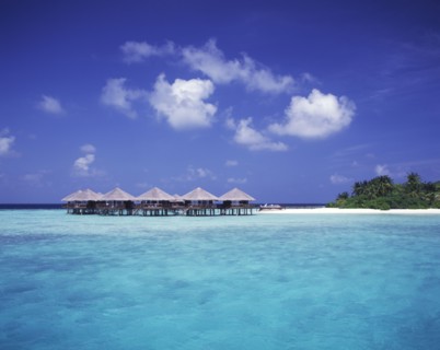 MALDIVES, Baros, "View across expanse of turquoise sea towards thatched beach huts on stilts, beach