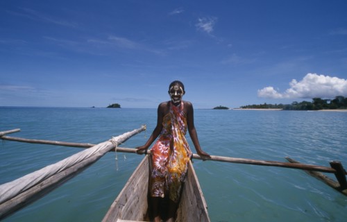 MADAGASCAR, Nosy Be, Young girl on a pirogue canoe wearing a colourful sarong and with her face