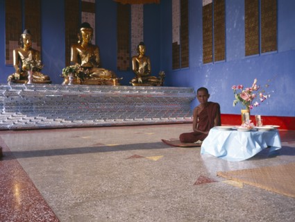 MYANMAR, Yangon, "Shwedagon Pagoda interior.  Monk sitting beside a raised altar with three seated,