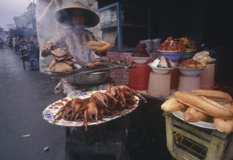 VIETNAM, Mekong Delta, Vinh Long, Woman cooking various meat products at market stall.