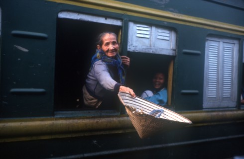 VIETNAM, Hai Van Pass, Old woman reaching out of the window of a train carriage with a straw hat in