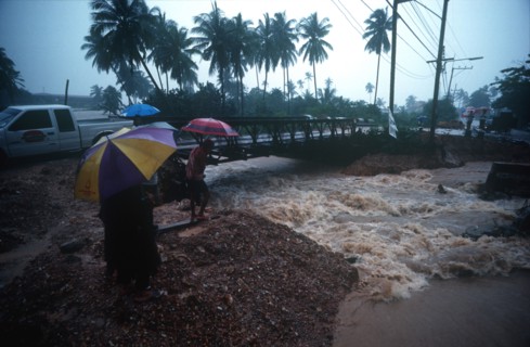 THAILAND, Ko Samui, "Torrent of flood water beneath bridge, watched by people with umbrellas. "