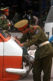 VIETNAM, Hanoi, Policeman leaning on the bonnet of a truck to write out a traffic ticket.