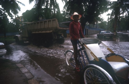 CAMBODIA, Phnom Pehn, Rickshaw and truck driving through a flooded street near the Royal Hotel