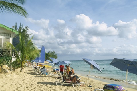WEST INDIES, Barbados, St Peter, Mullins Bay.  People on loungers with blue sun umbrellas on sandy