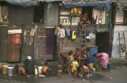INDIA, Maharashtra, Mumbai , Slum housing with group of children washing in buckets outside.