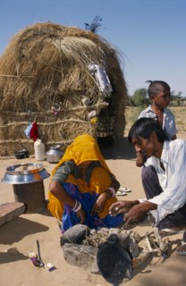 INDIA, Rajasthan, Work, Couple lighting a fire inside stone surround on sandy ground outside their