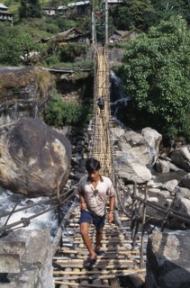 NEPAL, Annapurna Region, Marsyangdi River, Near Besisahar.  Young man crossing wood and rope foot