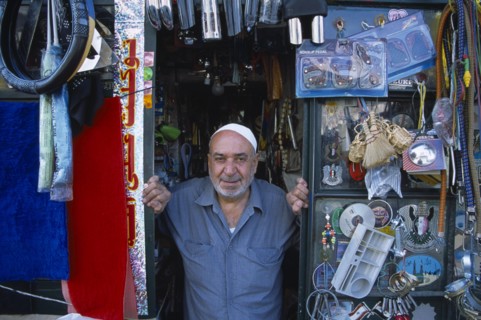 SYRIA, North, Halab, Male shopkeeper at the entrance to his shop with display of mixed goods