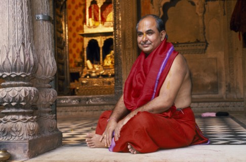 INDIA, Utter Pradesh, Vrindaven, Hindu priest in red robes sitting cross legged on temple floor.