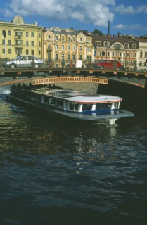 RUSSIA, St Petersburg, Moika Canal with tour boat passing underneath arched bridge with cars