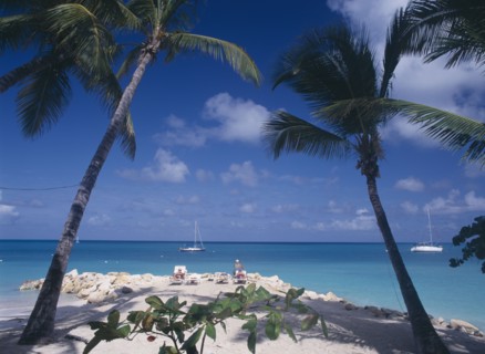 WEST INDIES, Antigua, Dickenson Bay, Sandy beach and rocks with people sunbathing on loungers and
