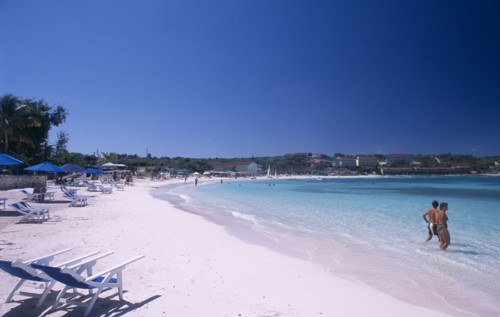 WEST INDIES, Antigua, Long Bay, Sandy beach beside bay with blue and white deckchairs and couple