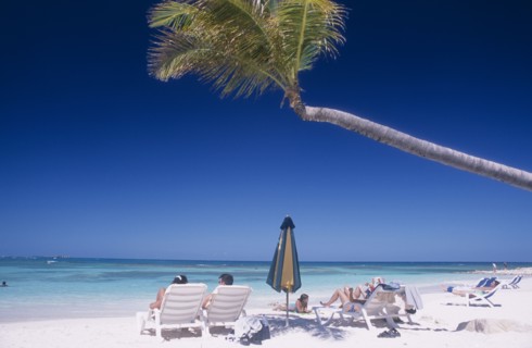 WEST INDIES, Antigua, Long Bay, Sandy beach overlooking bay with sunbathers on white sun loungers